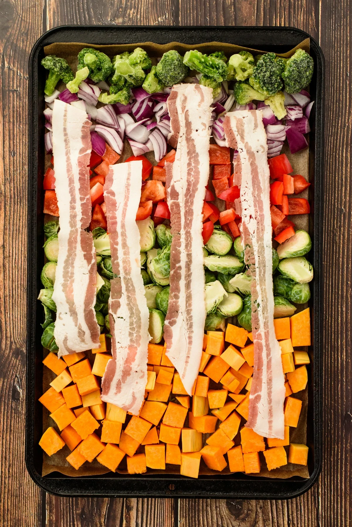 Vegetables on a sheet pan with slices of bacon on top.