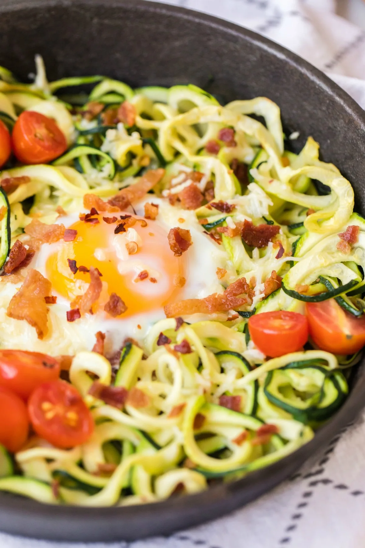 Close up of zucchini nest with runny egg, bacon, and tomatoes.