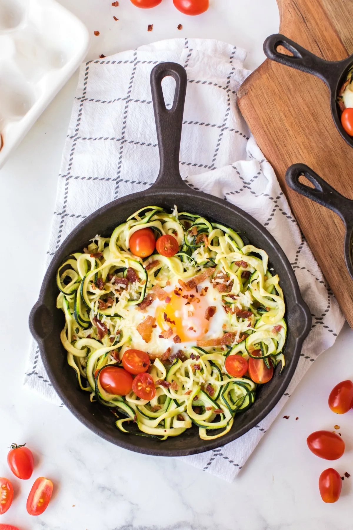 Zoodles with egg, bacon, tomato in a skillet.