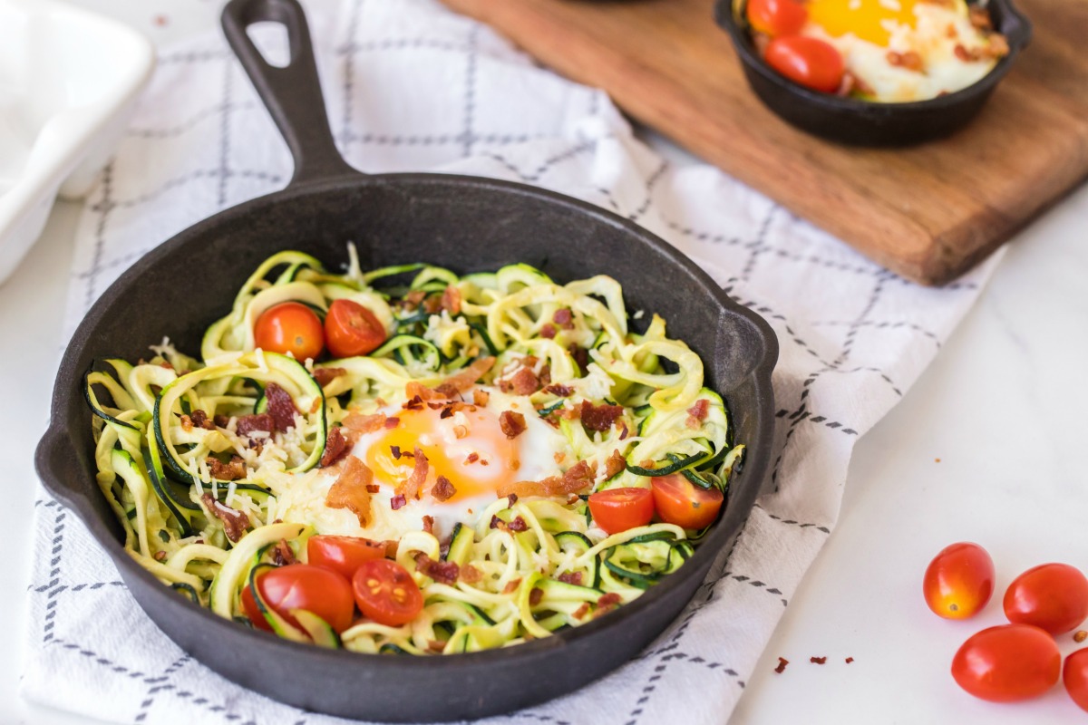 Zucchini nest in a skillet with bacon, egg, and tomatoes.