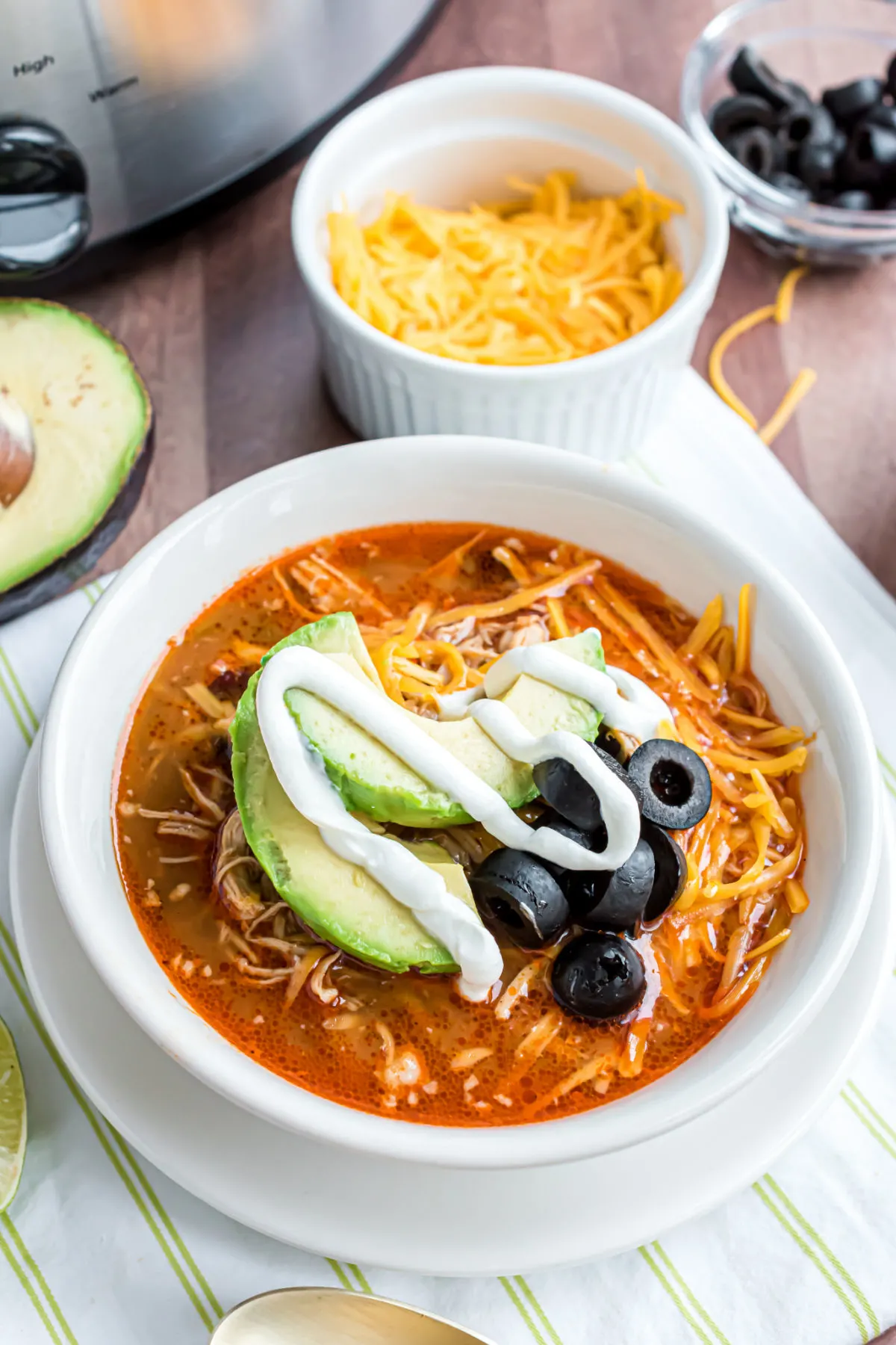 Bowl of chicken enchilada soup garnished with olives, avocado, and sour cream.