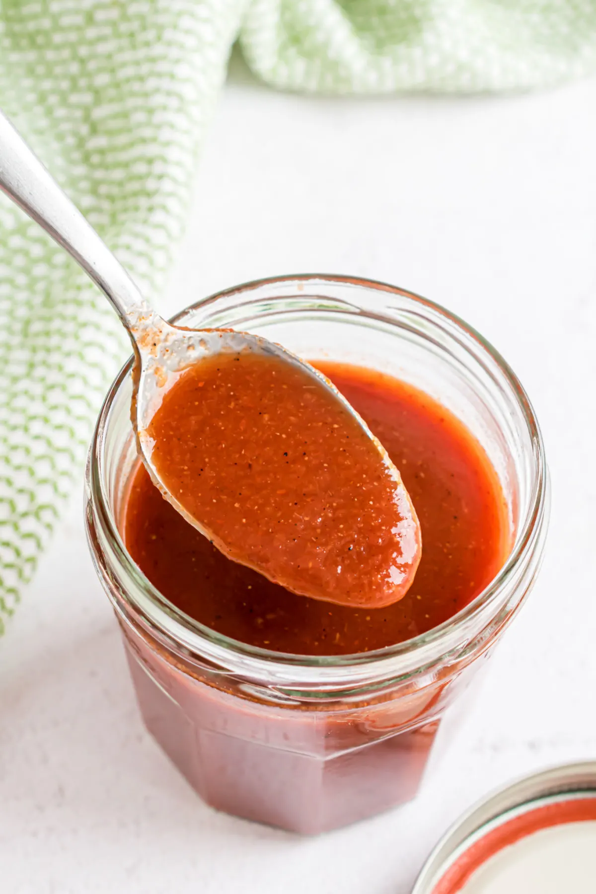 Homemade enchilada sauce in a jar with a spoon.
