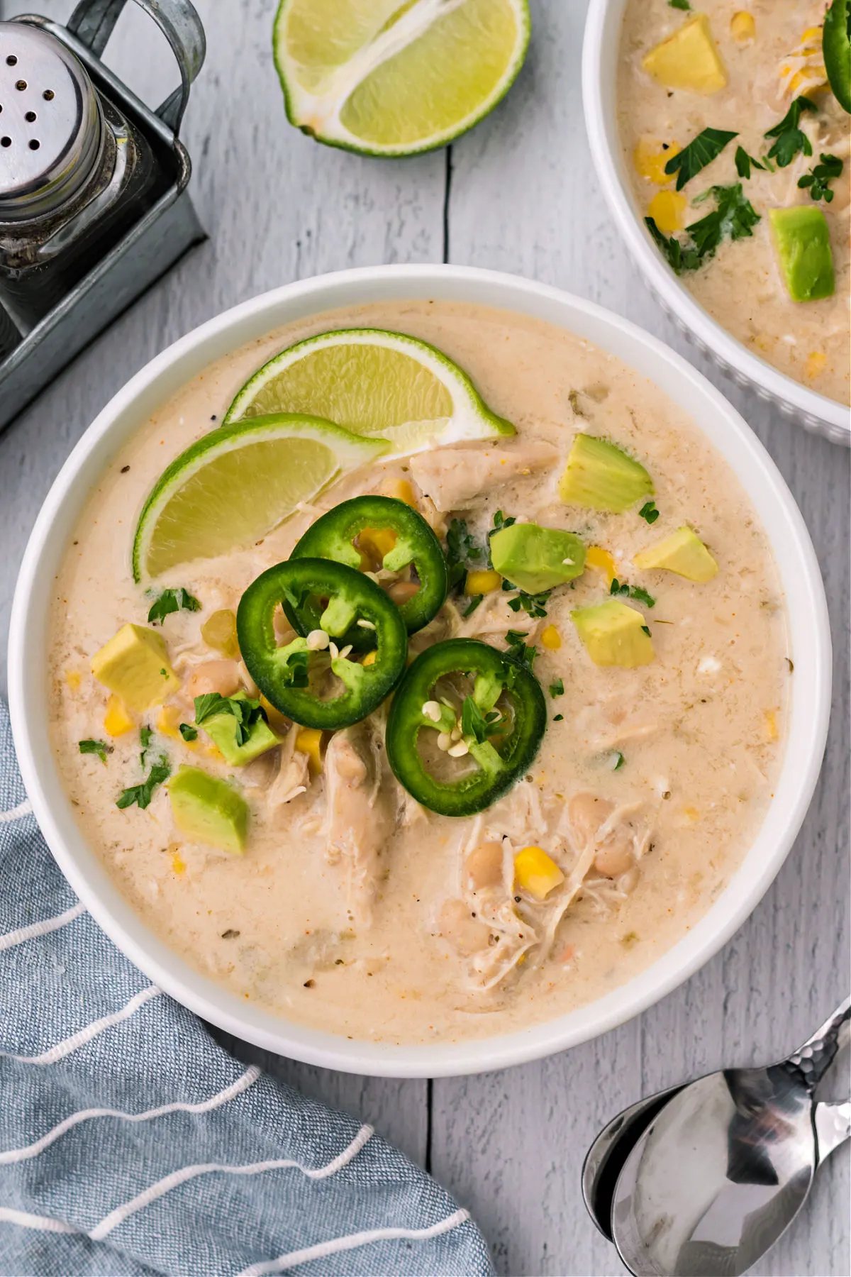 White chicken chili garnished with lime and jalapeno in white bowl.