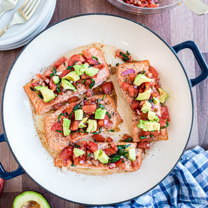 Bruschetta topped baked salmon with avocado in a skillet.
