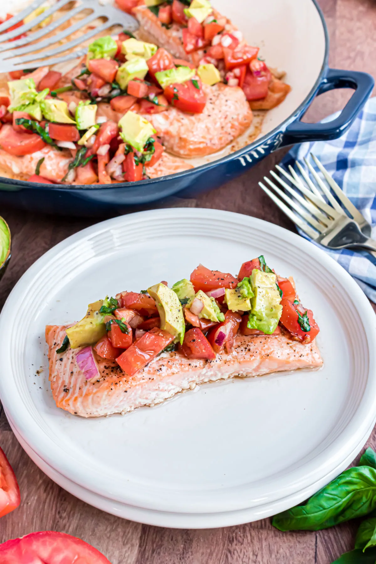 Salmon filet topped with bruschetta and avocado on a white dinner plate.
