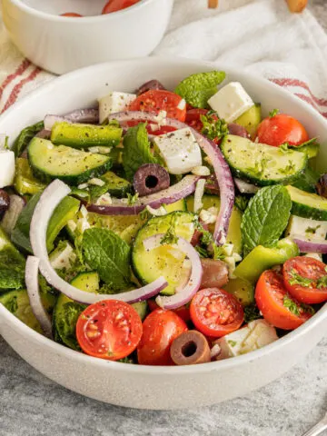 Fresh salad in a white bowl with greek dressing.
