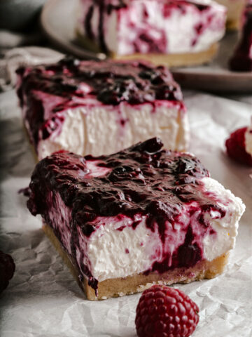 No bake cheesecake bars with a berry topping on parchment paper.