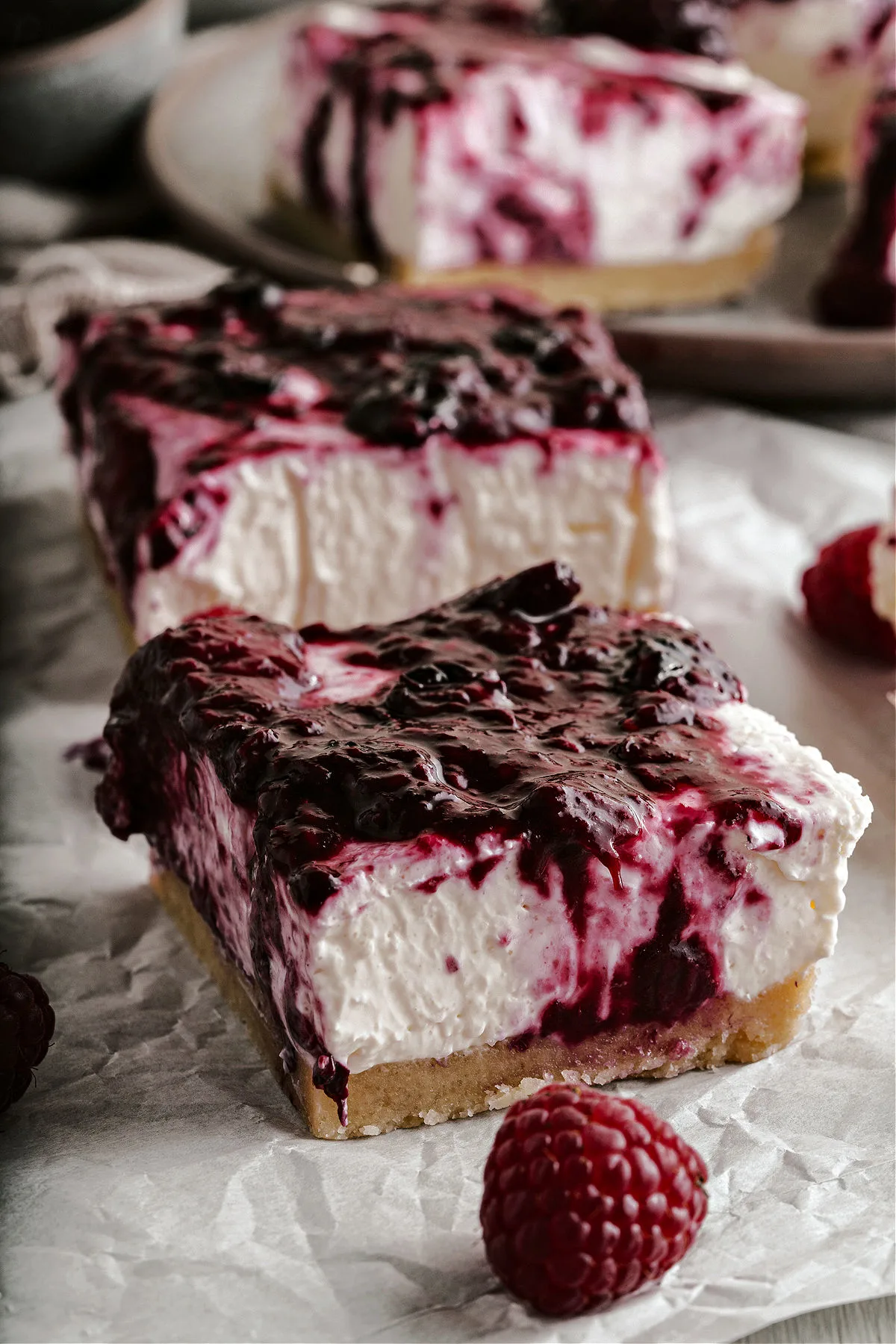No bake cheesecake bars with a berry topping on parchment paper.