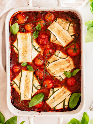 Zucchini rolled up with cheese and marinara sauce in white baking dish.