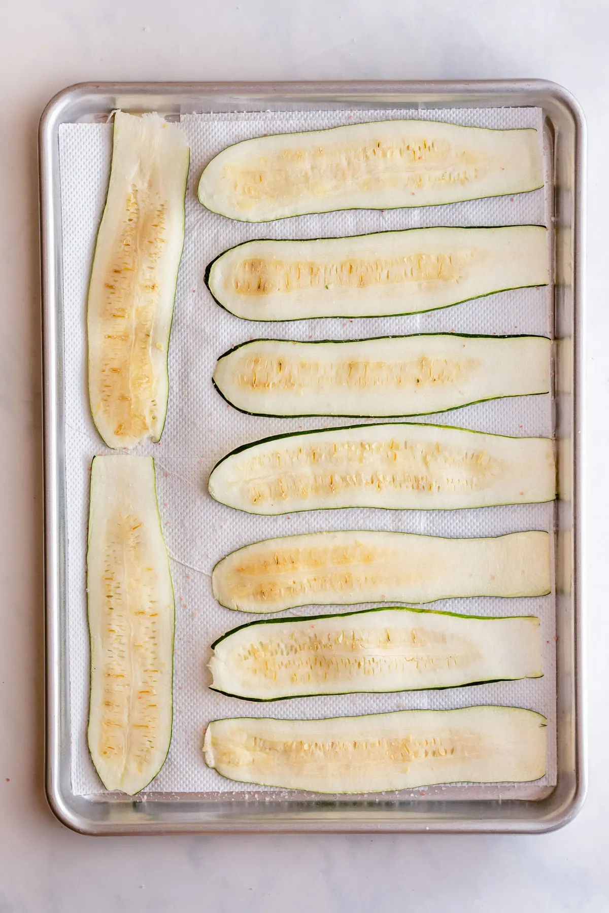 Zucchini strips on paper towel lined baking sheet and salted to remove moisture.