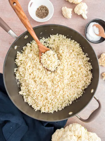 Riced cauliflower cooked in a skillet with wooden spoon.