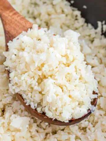 Cauliflower rice in a skillet on a wooden spoon.
