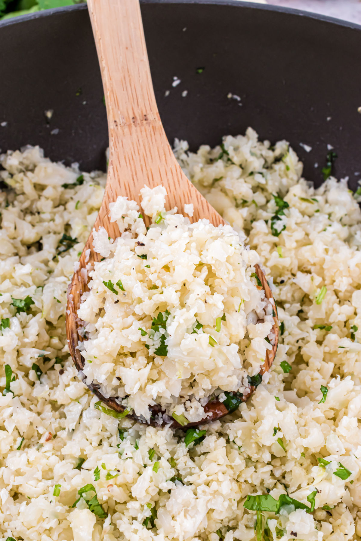 Cilantro lime cauliflower rice in a skillet with wooden spoon.