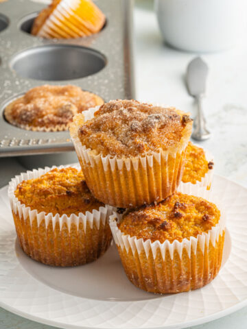 Stack of three pumpkin muffins in white wrappers.