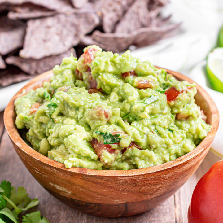 Wooden bowl with chunky guacamole and blue corn tortilla chips.