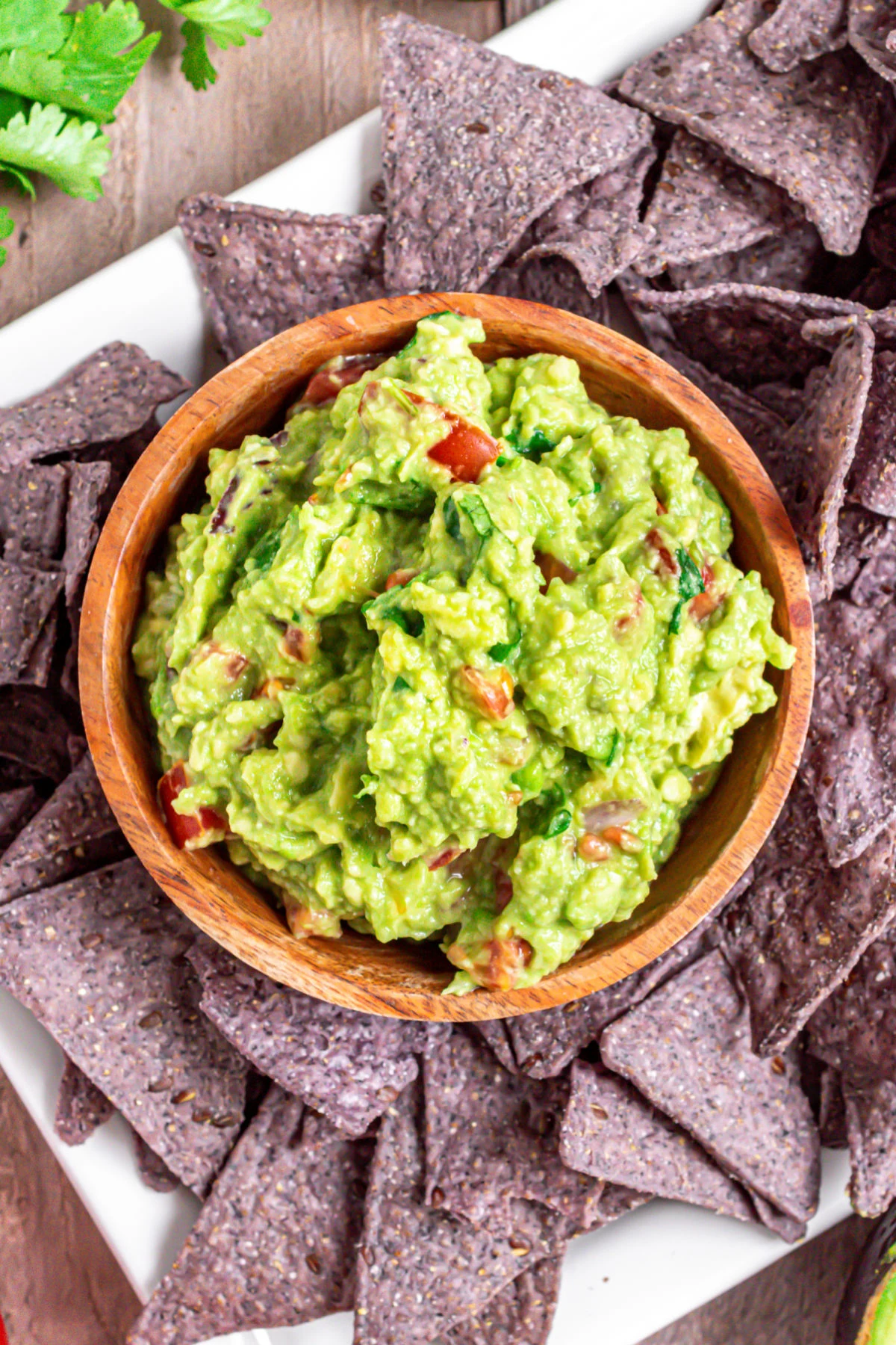 Guacamole in wooden bowl served with blue corn chips.