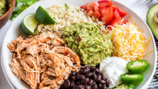 A white bowl with chicken taco ingredients, including cauliflower rice, beans, guacamole, and more.