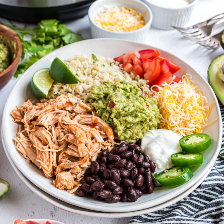 A white bowl with chicken taco ingredients, including cauliflower rice, beans, guacamole, and more.