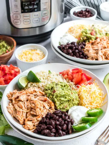 Chicken taco bowl with cheese, guacamole, black beans assembled in a white bowl with Instant Pot in background.