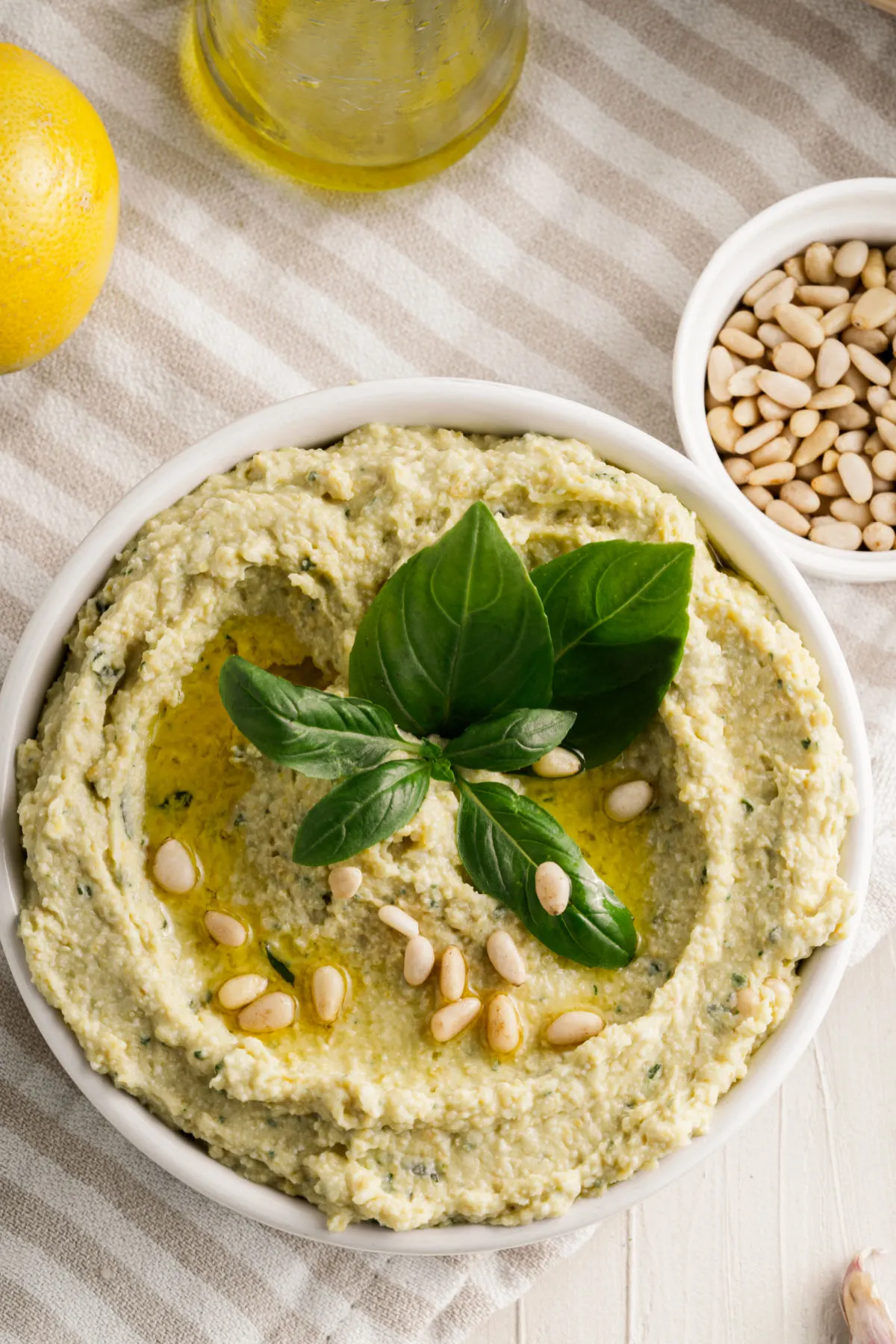 Pesto hummus in a bowl with basil and pine nuts for garnish.