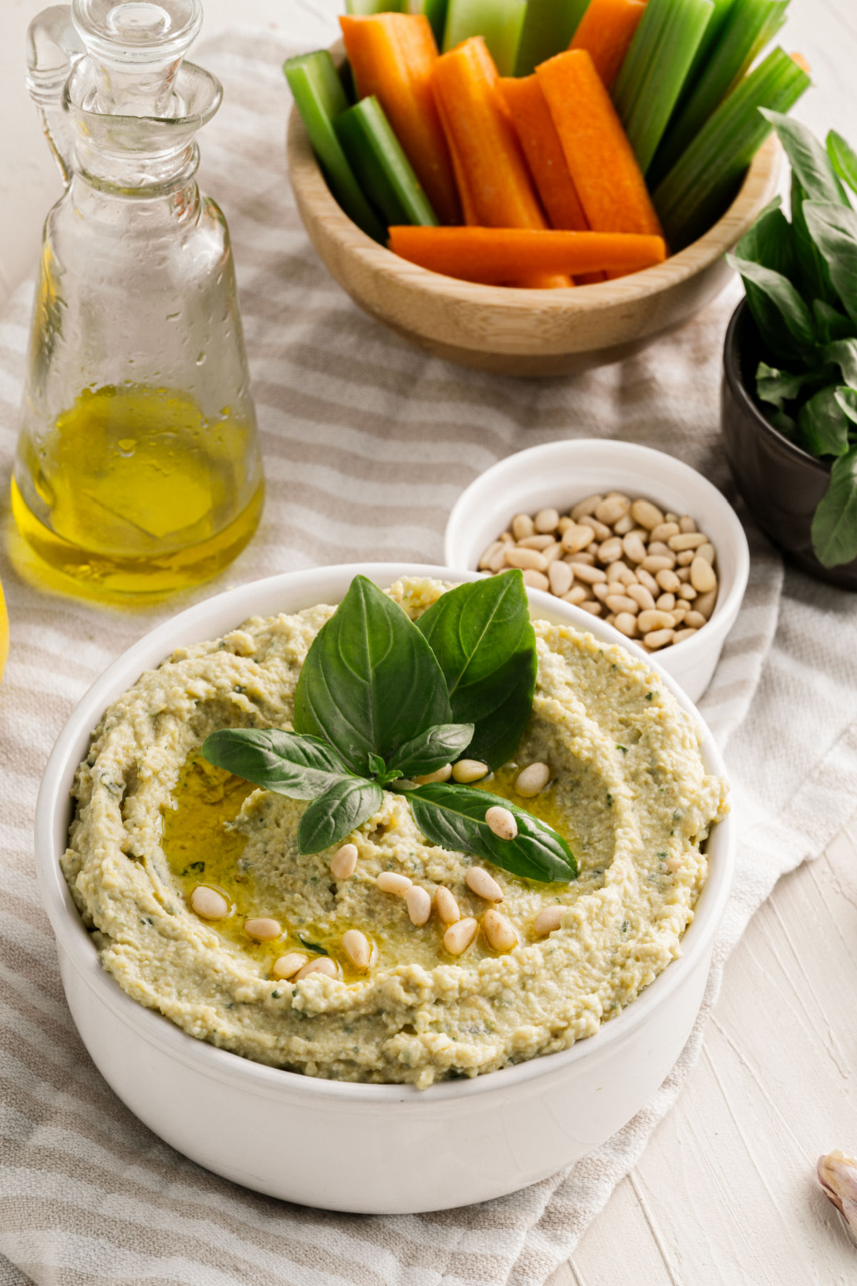 Pesto hummus in a white bowl with a side of carrot sticks.