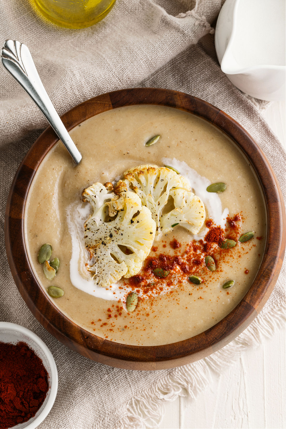 Wooden bowl with cauliflower soup topped with cream, paprika, and pepitas.