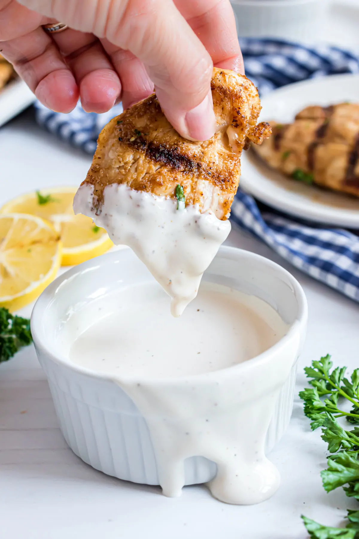 Grilled chicken tenders being dunked in a bowl of ranch dressing.
