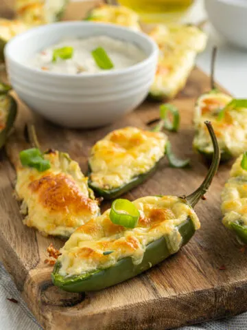 Baked jalapeno poppers on a wooden cutting board with a bowl of ranch,