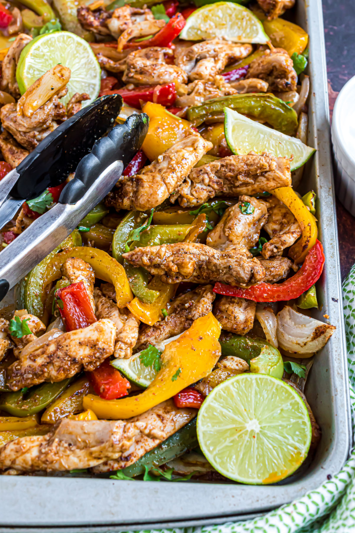 Sheet pan chicken fajitas baked and served with tongs and fresh limes.