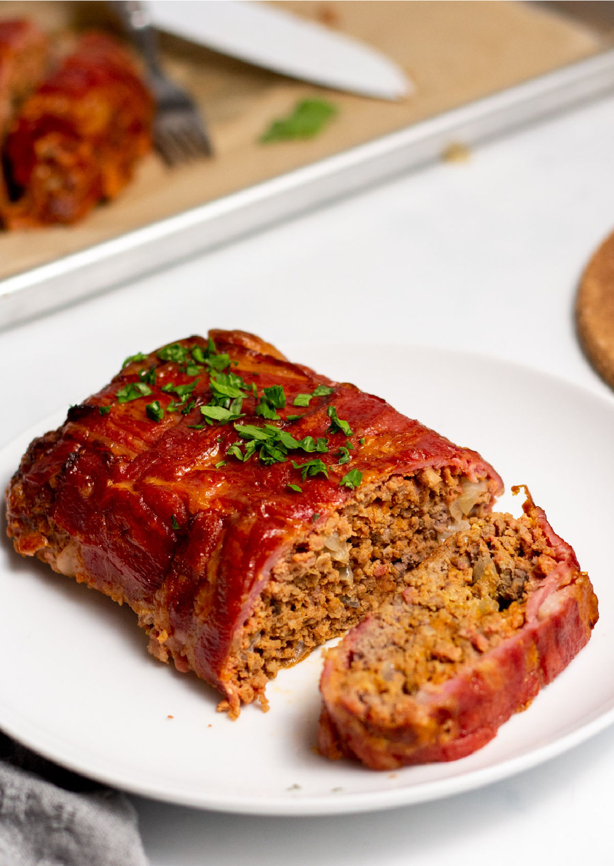 Bacon wrapped meatloaf on a white serving plate.