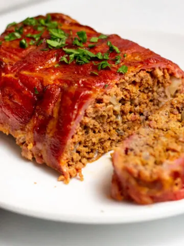 Bacon wrapped meatloaf served on a plate with a slice cut out.