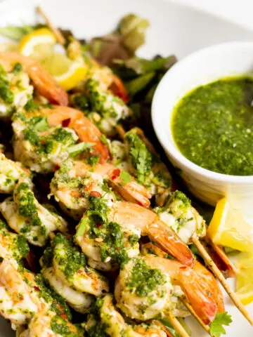 Grilled chimichurri shrimp kabobs, served with chimichurri sauce on the side in a bowl.