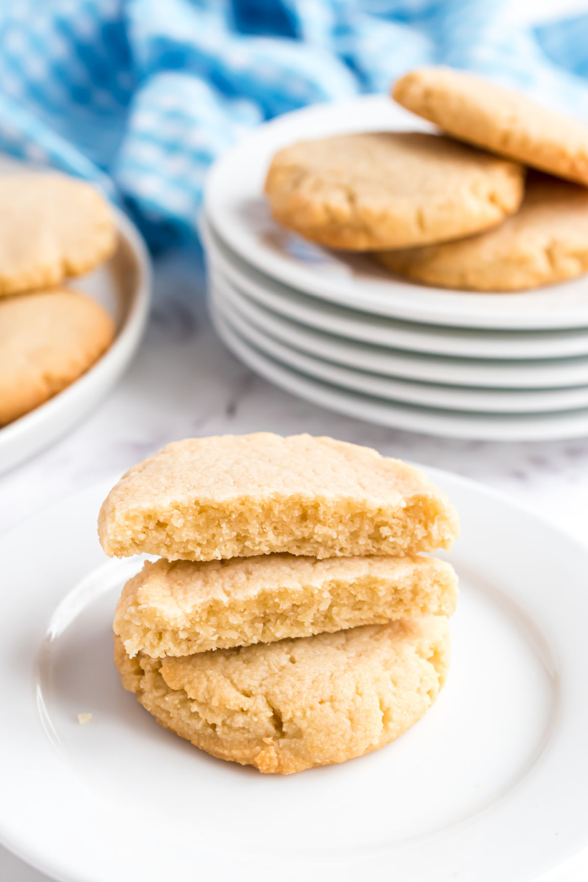 Shortbread cookies stacked on a white plate with one broken in half.