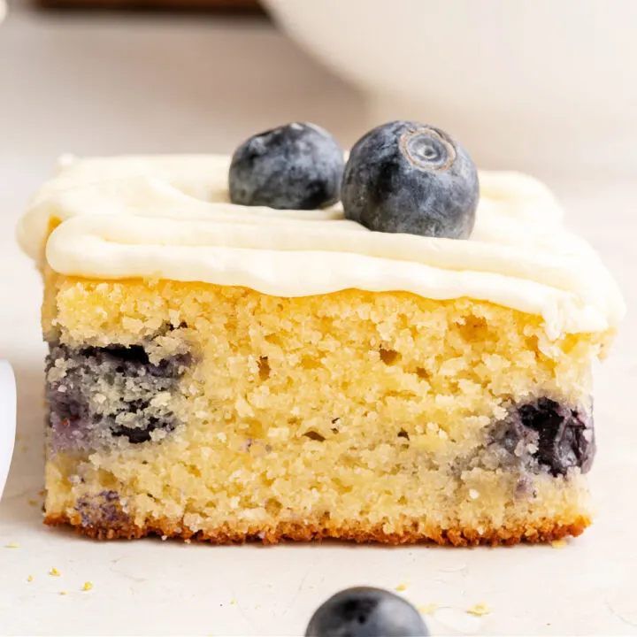 Slice of blueberry cake with lemon frosting on a white plate.