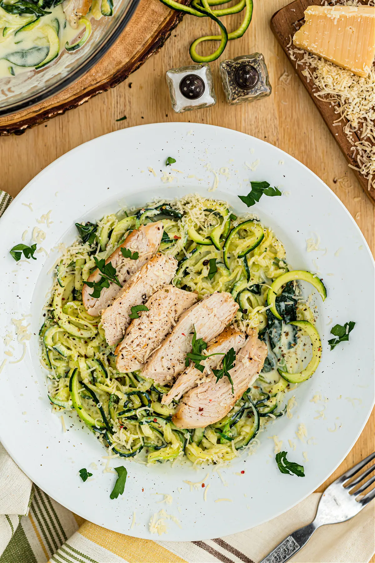 Zoodles topped with chicken and alfredo sauce on a white dinner plate.