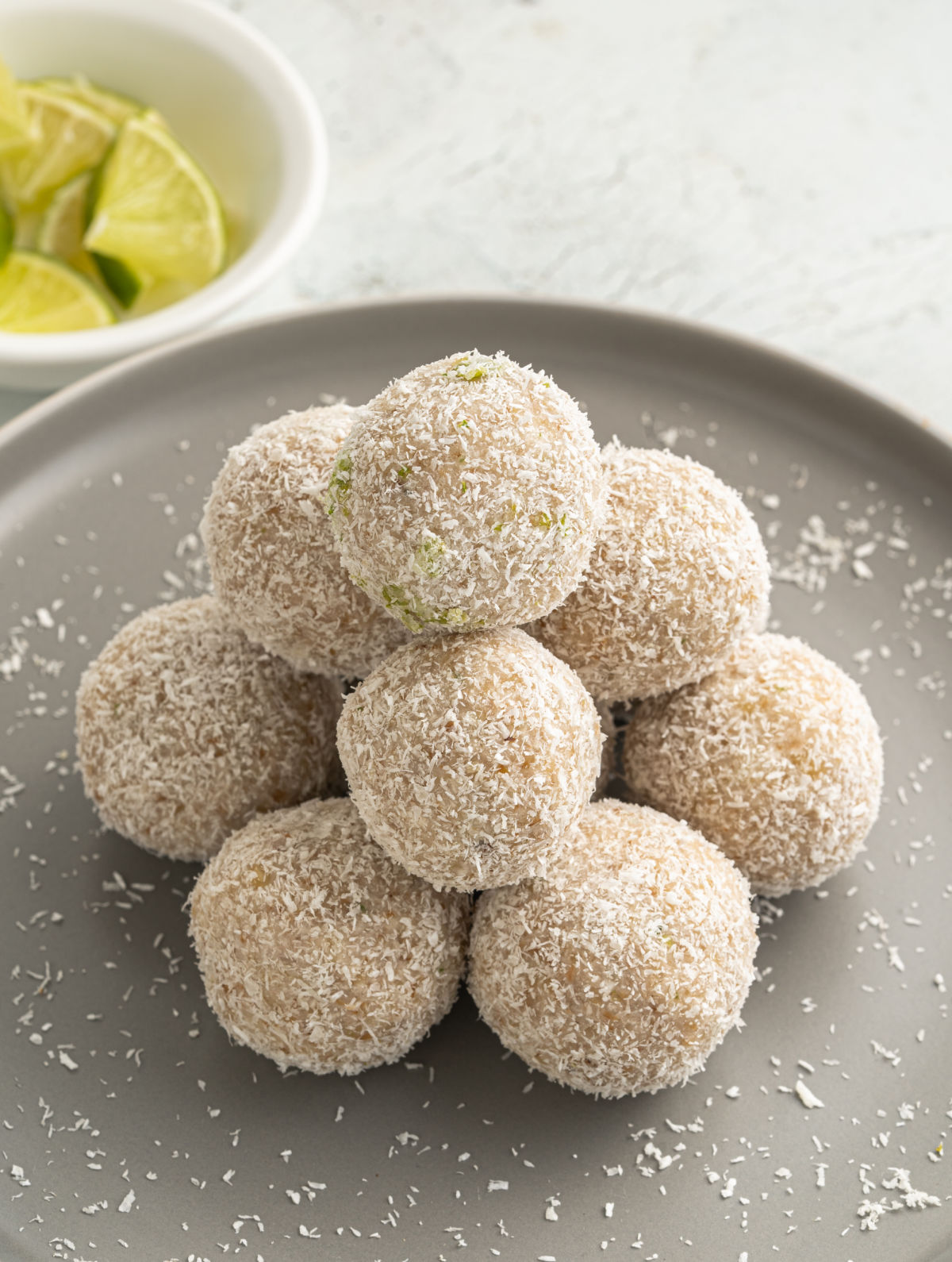 Coconut lime energy balls stacked on a gray plate.