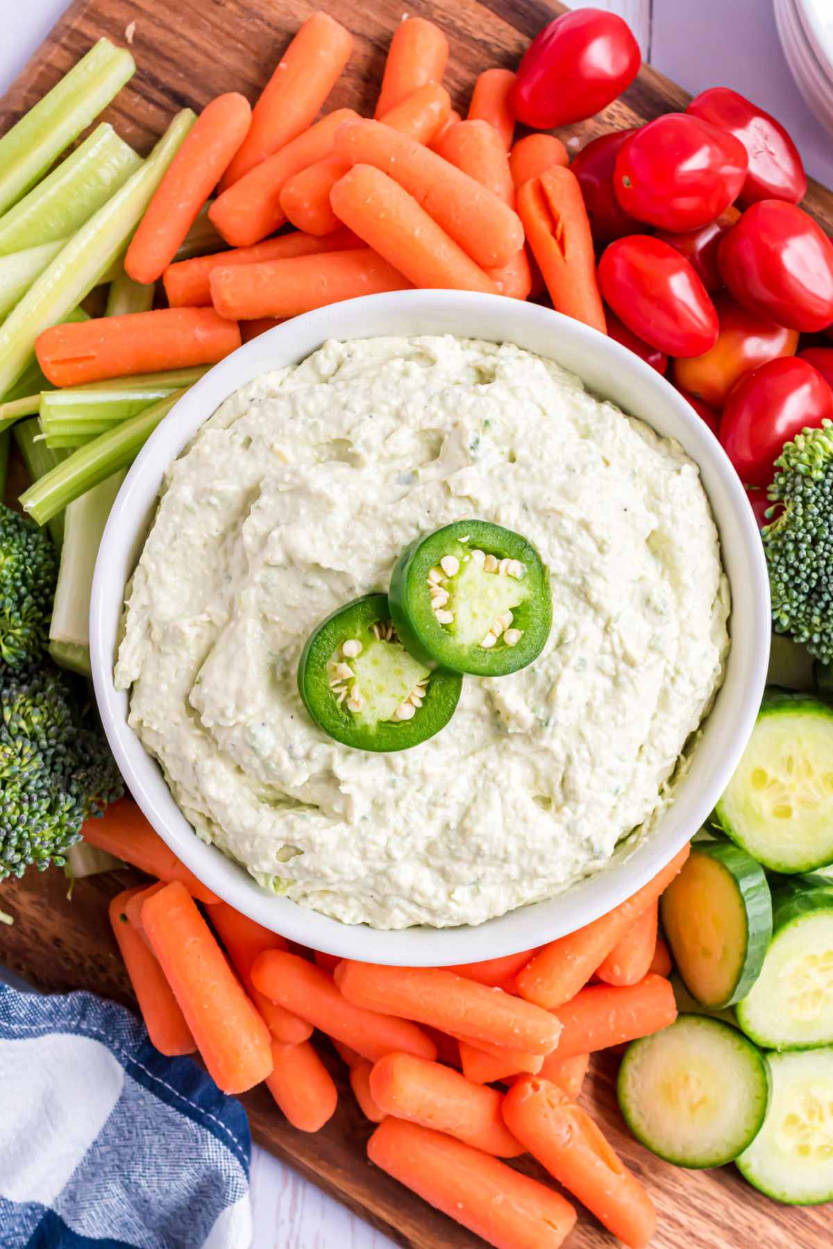 Jalapeno artichoke dip served in a white bowl with fresh vegetables.