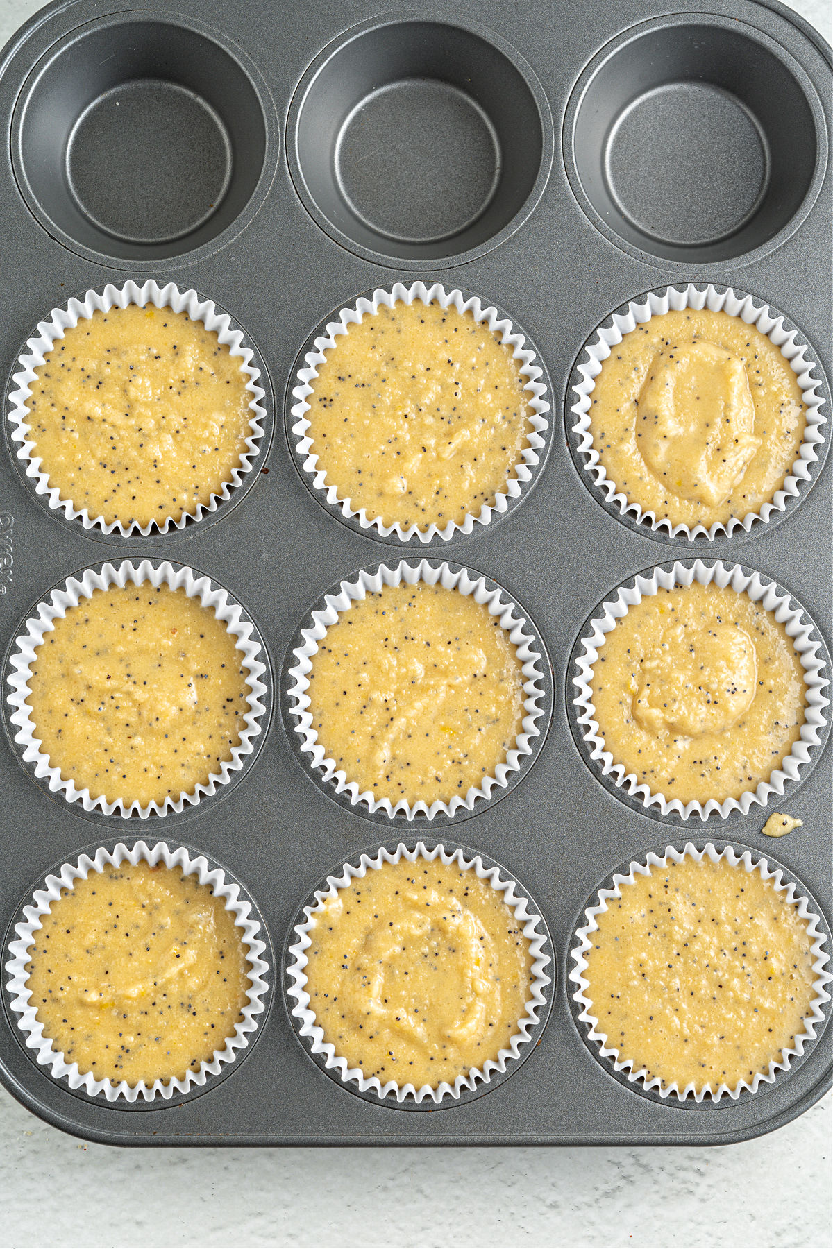 Lemon muffin batter unbaked in a cupcake tin.