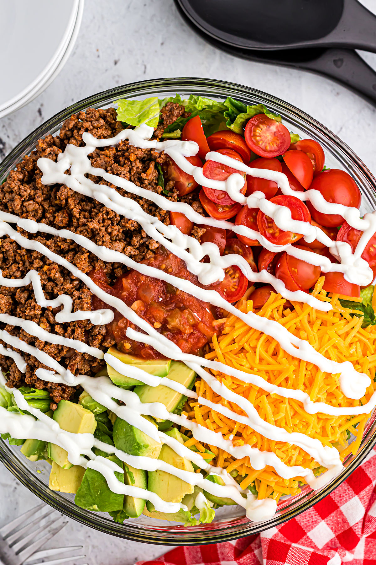 Taco salad ingredients arranged in a serving bowl and drizzled with sour cream.
