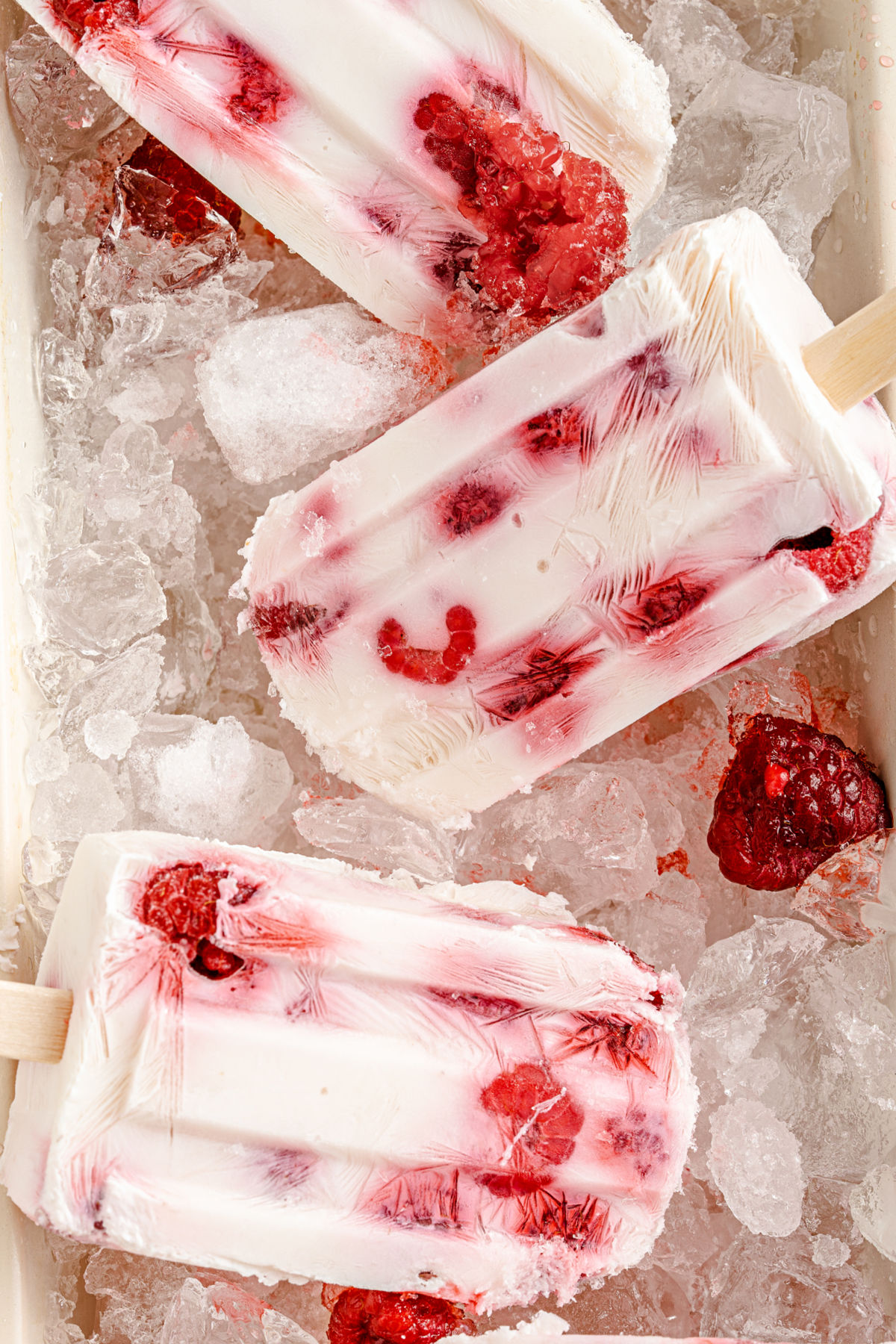 Yogurt popsicles with raspberries on a pan of ice.