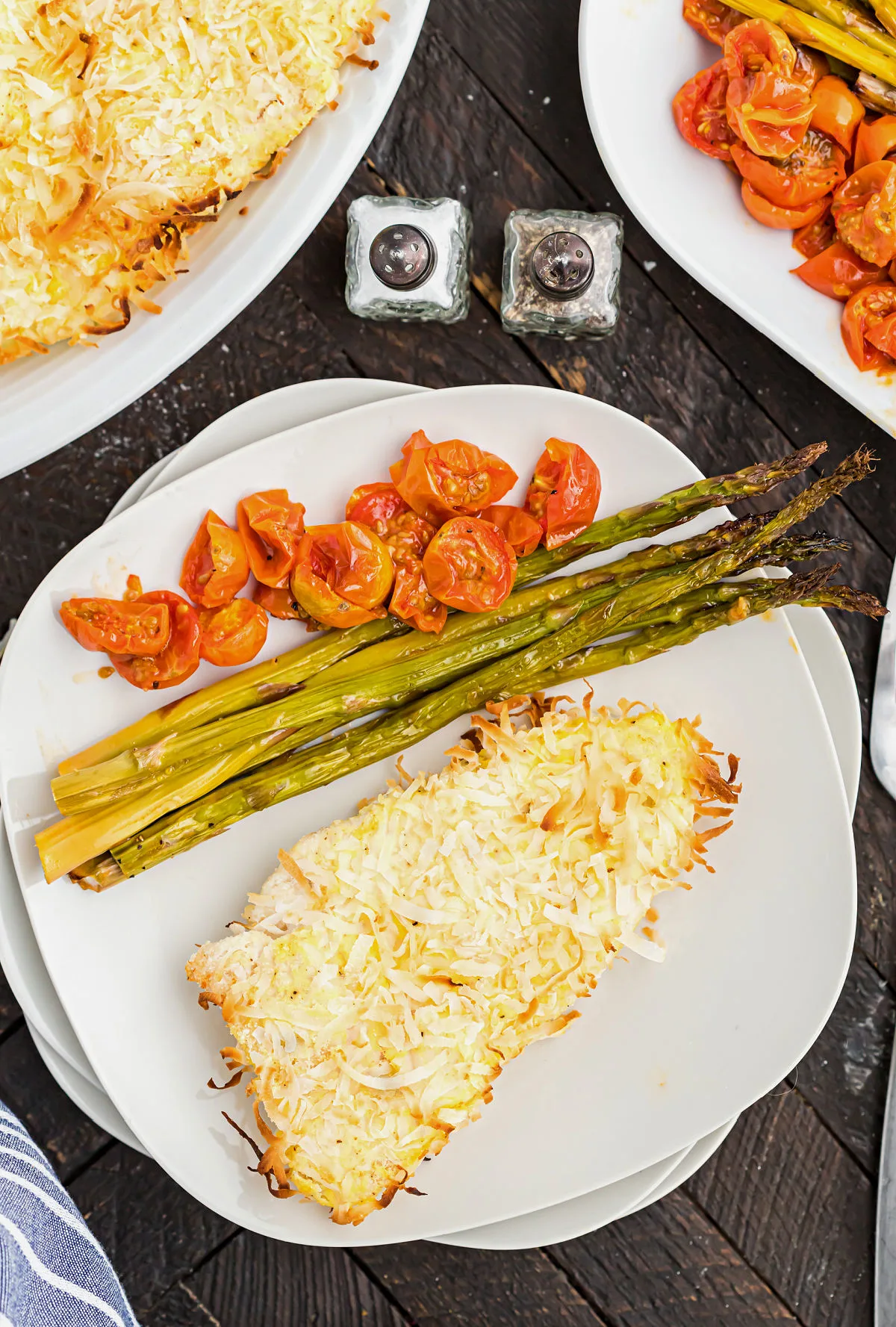 Coconut chicken on a dinner plate with roasted tomatoes and asparagus.