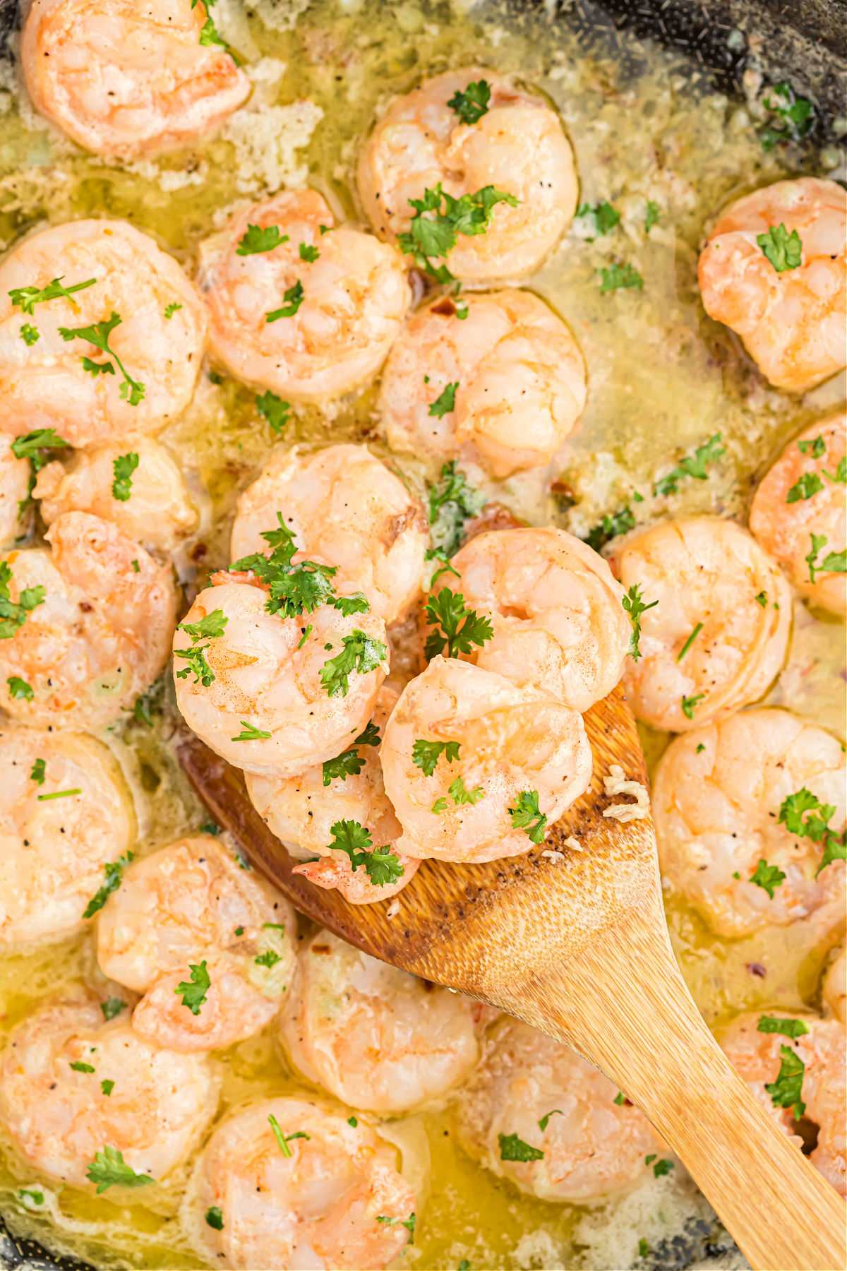 Garlic butter shrimp cooked in a skillet and served with a wooden spoon.