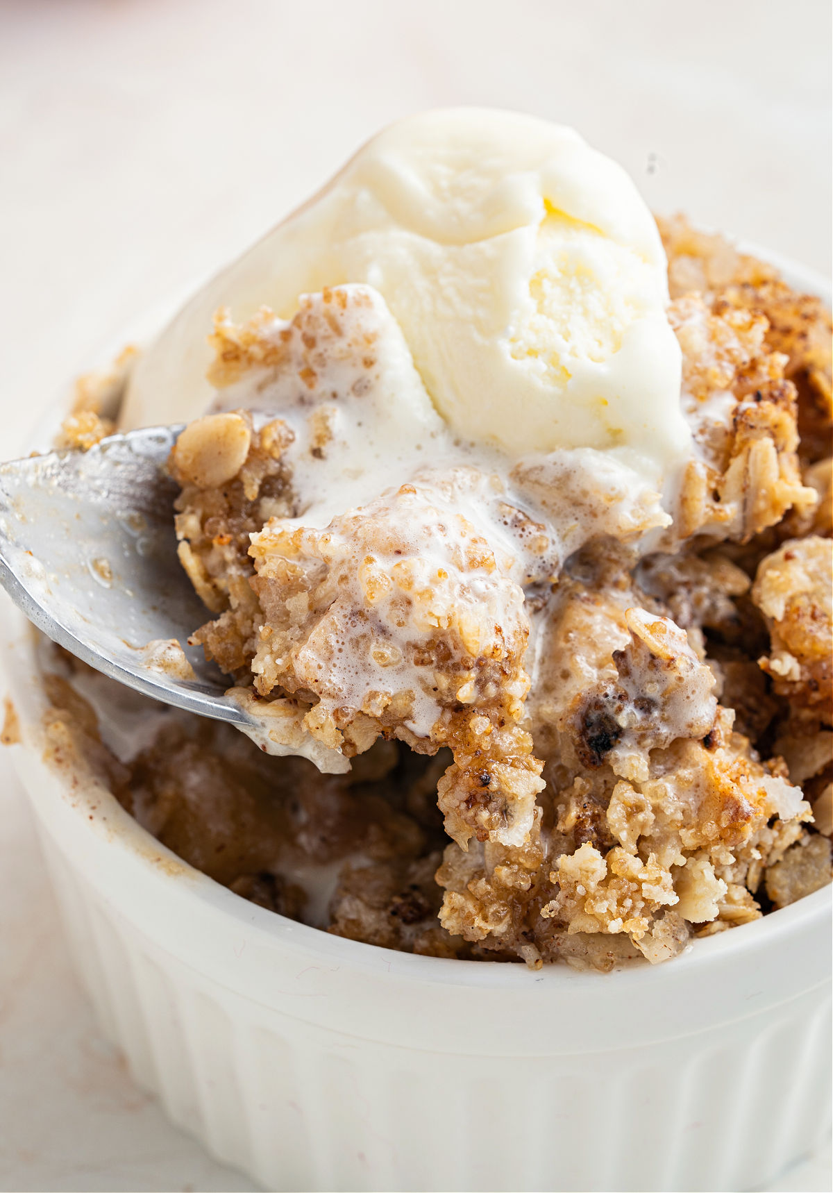 Apple crisp served with vanilla ice cream in a white bowl.