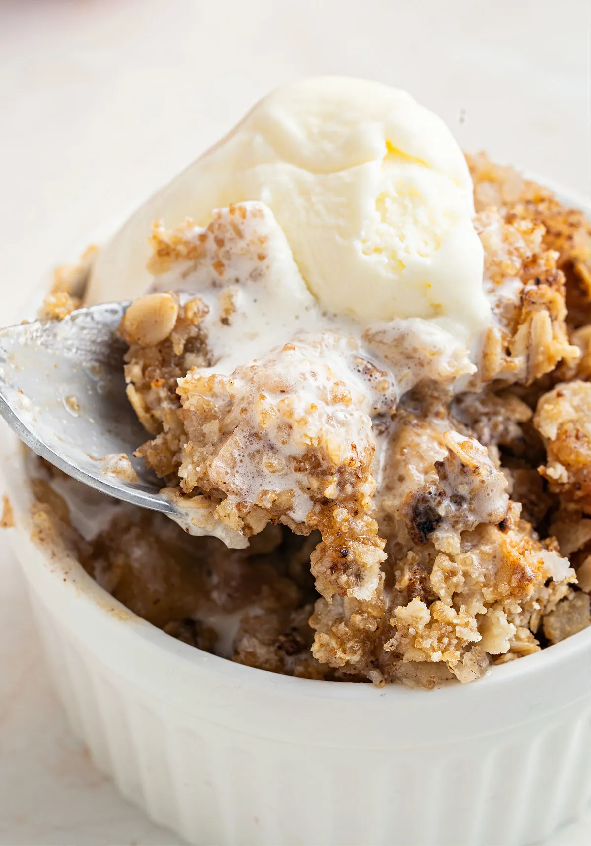 Apple crisp served with vanilla ice cream in a white bowl.
