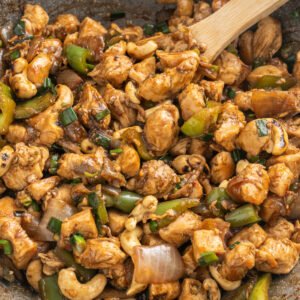 Cashew chicken stir fry in a skillet with wooden spoon.