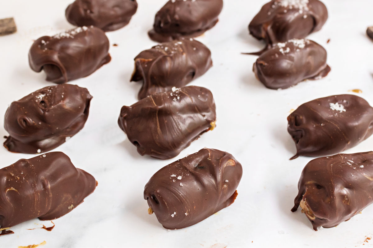 Chocolate covered dates stuffed with peanut butter on a piece of parchment paper.