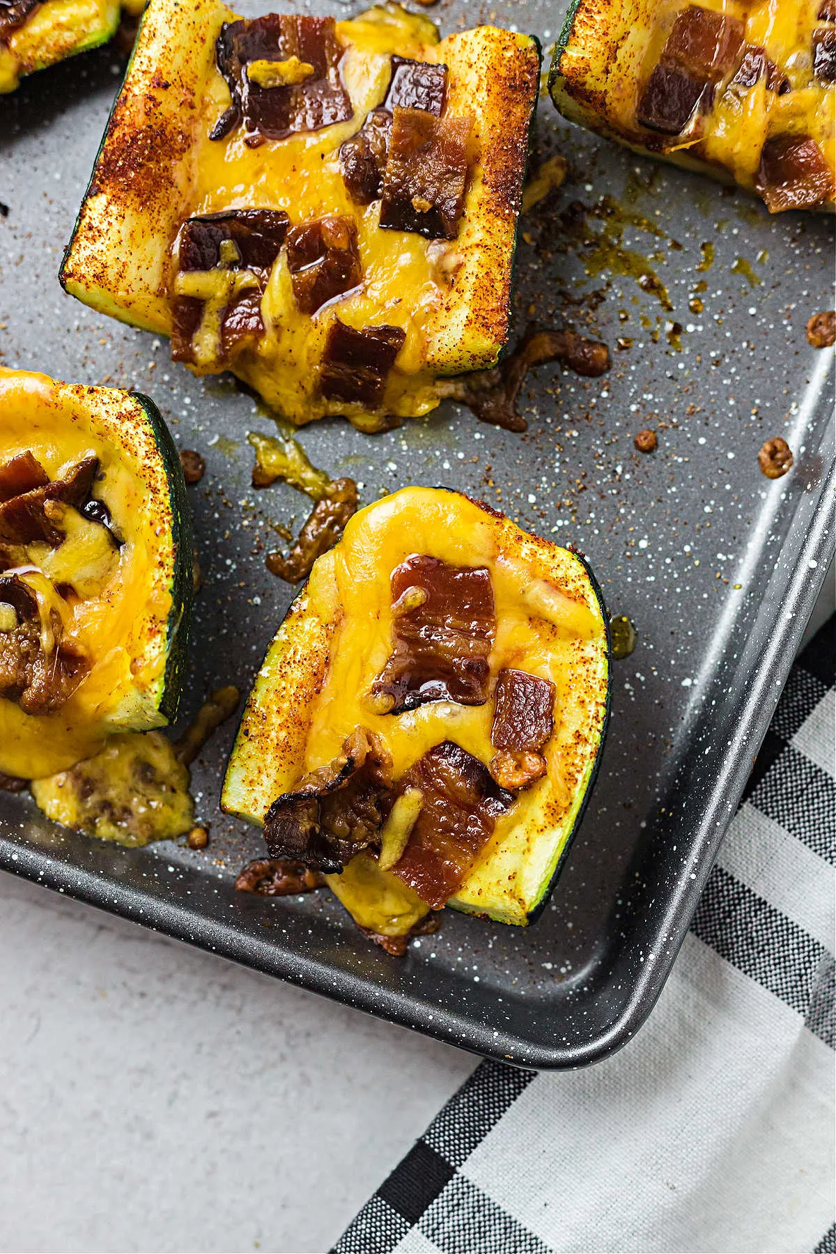 Baked zucchini skins on a cookies sheet with melted cheese and bacon.